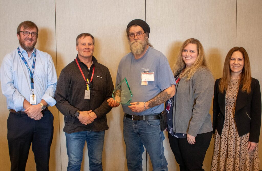 Employee holds his award alongside other people.