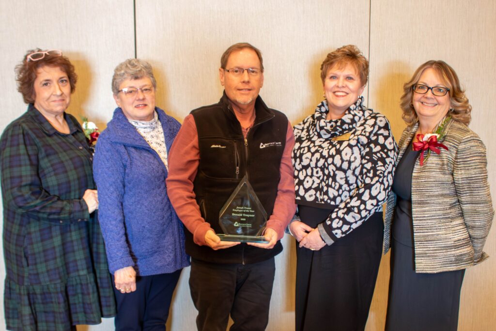 An employee holds his award alongside other people.